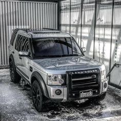 an suv parked in front of a building with snow on the ground and metal walls behind it