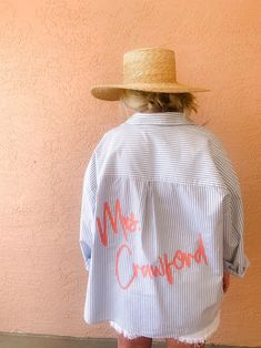 a woman wearing a white shirt with pink writing on it and a straw hat over her head