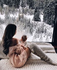 a woman sitting on top of a bed in front of a window holding a cup