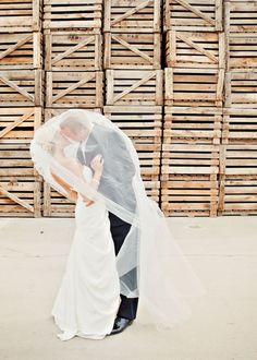 a bride and groom standing under a veil in front of stacks of wooden pallets