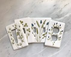 three ceramic switch plates with plants painted on them sitting on a marble countertop next to each other