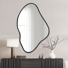 a mirror on the wall above a dresser with a vase and lamp next to it