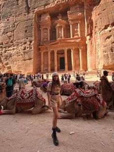 a woman standing next to camels in front of a large building with people around it