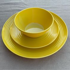 a yellow bowl and plate set on a gray tablecloth with a white cloth in the background