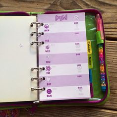 an open planner book sitting on top of a wooden table next to markers and pens