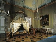 an old fashioned bedroom is decorated in green and gold colors with chandelier, bed, dressers, and paintings