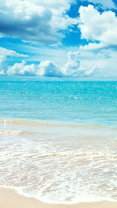 an ocean view with waves crashing on the beach and clouds in the blue sky above