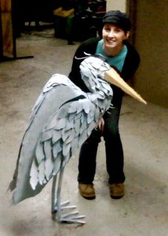 a man standing next to a statue of a pelican holding a large bird's beak