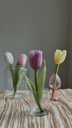 three glass vases with tulips in them sitting on a tableclothed surface