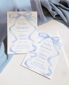 two baby shower cards sitting on top of a blue cloth covered tablecloth next to a folded sheet