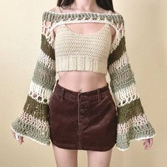 a woman wearing a crochet top and brown skirt standing in front of a wall