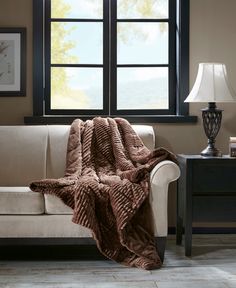 a couch with a blanket on it next to a lamp and window in a living room