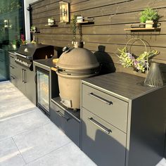 an outdoor bbq grill with potted plants on the counter and outside wall behind it