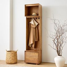 a wooden cabinet with clothes hanging on it and a basket next to it, in front of a white wall