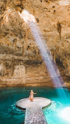 two people are standing on a rock in the middle of a pool with blue water