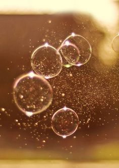 three bubbles floating in the air on top of a brown surface with water droplets around them