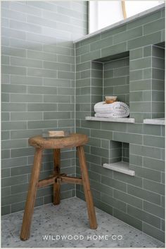 a wooden stool sitting in front of a green tiled bathroom wall next to a window