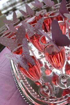 there are many wine glasses on the table with paper butterflies in them and one glass is filled with pink liquid