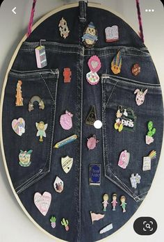 the back side of a denim jacket with patches and pins attached to it, hanging on a wall