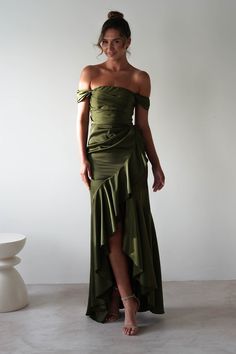 a woman wearing a green dress standing in front of a white wall with her hands on her hips