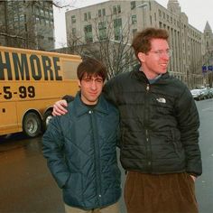 two men standing next to each other in front of a bus