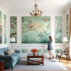 a woman standing in a living room next to a blue couch and table with flowers on it