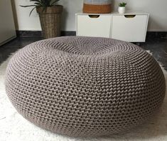 a large round knitted ottoman sits on the floor in front of a white cabinet and potted plant