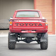 a red toyota pickup truck parked in a parking lot next to a building with the word toyota written on it