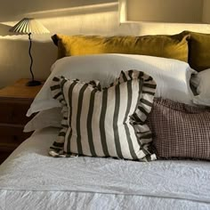 a bed topped with lots of pillows on top of it's headboard next to a night stand