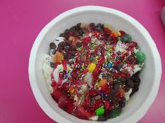 a white bowl filled with lots of candy and sprinkles on top of a pink table