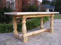 a wooden table sitting on top of a cement ground next to green grass and bushes