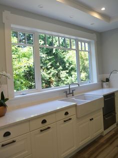 an empty kitchen with white cabinets and counter tops, has a large window overlooking the trees outside