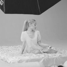 a woman sitting on top of a bed with an umbrella over her head in the background