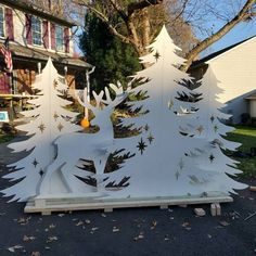 a white christmas tree is standing in front of a house with trees and snowflakes on it