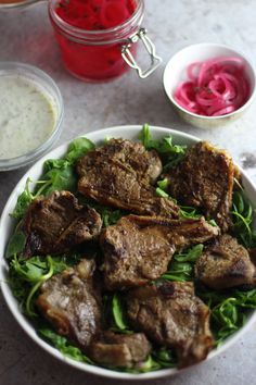 a white bowl filled with meat and lettuce next to sauces on a table