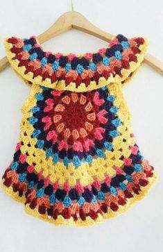 a colorful crocheted dress hanging on a wooden hanger with a white wall in the background