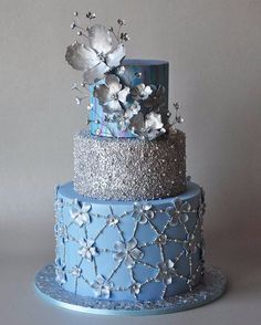 a three tiered blue and silver cake with flowers on top