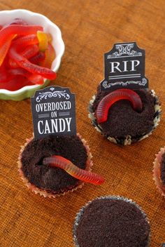 cupcakes decorated with worms and candy are on a table next to a bowl of peppers