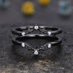 two black gold wedding rings with white diamonds on the top and bottom, sitting on a stone surface