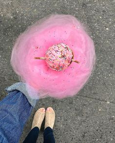 a pink donut with sprinkles sitting on top of it next to someone's legs