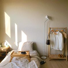 an unmade bed in a small room with clothes hanging on the rack and other items