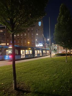 a train traveling down tracks next to a lush green field at night with buildings in the background