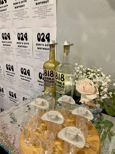 a table topped with lots of glasses next to a bottle of alcohol and some flowers