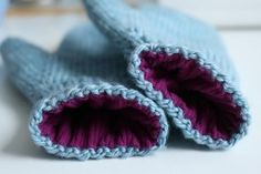 two blue knitted baby mittens sitting on top of a white table next to each other