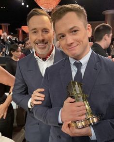 two men standing next to each other holding trophies