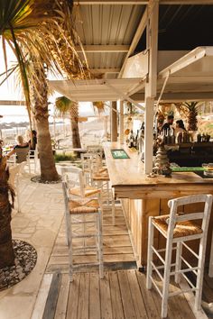 an outdoor bar with wooden tables and chairs under a palm tree on the beach side