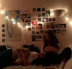 two people sitting on a bed with lights strung over the head and posters above them