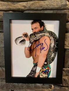 a man with a snake on his back in front of a stone wall holding a large snake