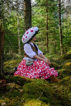 a woman in a red and white polka dot dress sitting on the ground next to trees