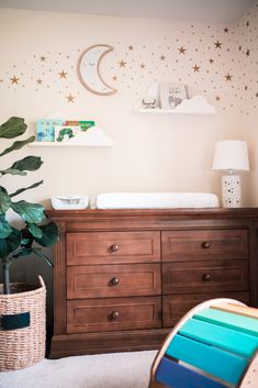 a baby's room with a crib, dresser and potted plant